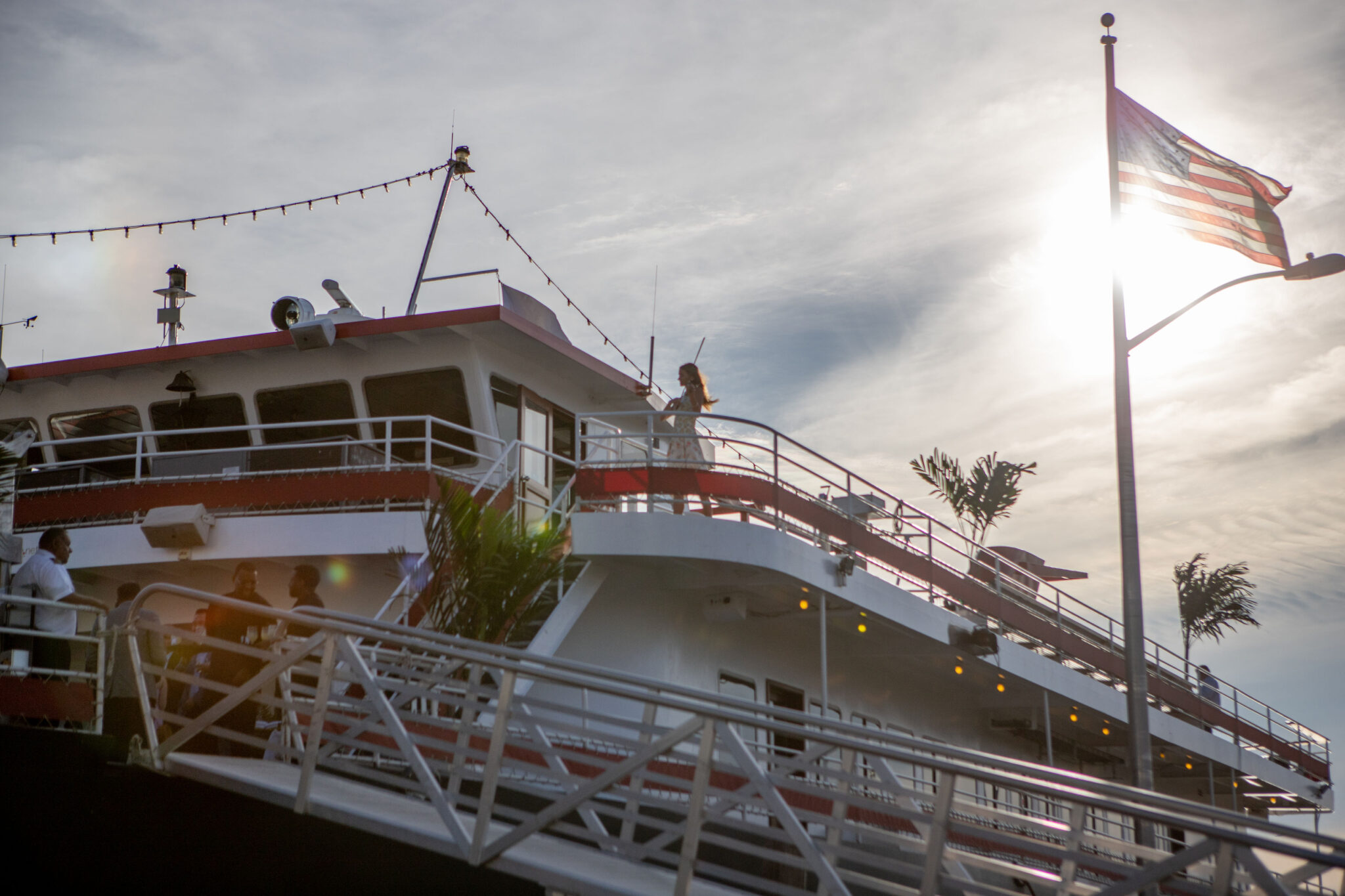 View of the Media.net event yacht at sunset, with an American flag in the foreground and a violinist visible on the upper deck.