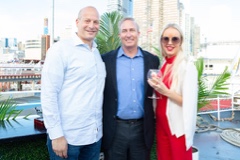 Three event attendees posing together on the yacht deck with city buildings in the background.