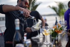 Bartender pouring white wine during the Media.net yacht party, with decorated glasses and palm accents at the bar.