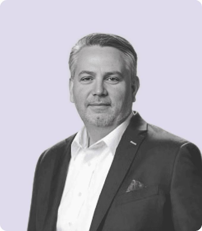 Black-and-white portrait of Ken Lagana, CRO of Media.net, with a friendly, professional demeanor, wearing a suit jacket and a white shirt against a muted lavender background.