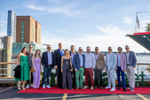 Group of Media.net team members and guests posing on a dock at the 'Cannes on the Hudson' yacht party, part of a digital advertising industry celebration in NYC